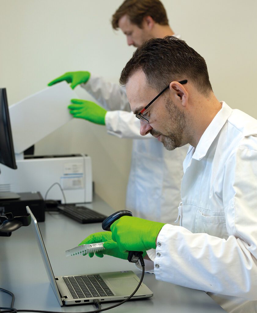 Senior onderzoeker Eric Fakket scant een monster in voor registratie in het LIMS, met op de achtergrond collega Marcel de Winter
